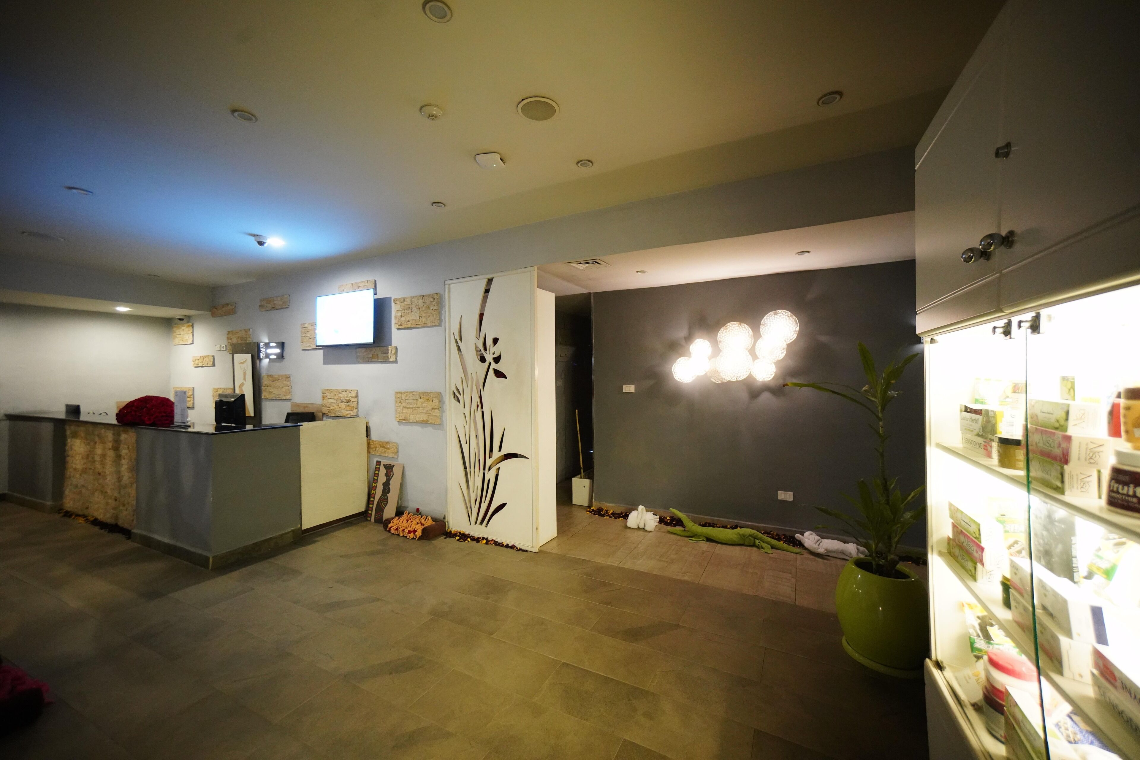 Un área de recepción con mostrador, televisor, lámpara de pared y un refrigerador con artículos en su interior.