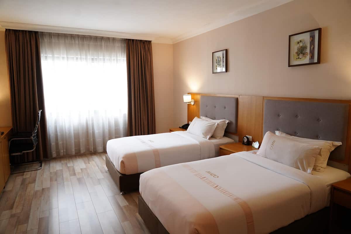 Habitación de hotel con dos camas, un escritorio, una silla y una ventana con cortinas.