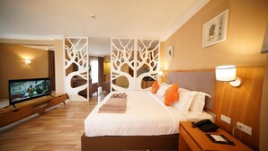 Una habitación de hotel con cama, televisión, mesita de noche de madera y lámpara de pared.