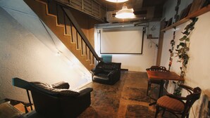 A room with a staircase, a black leather sofa, a wooden dining table with chairs, and a whiteboard on the wall. - PITO BEPPU hostel & cafe (Beppu)