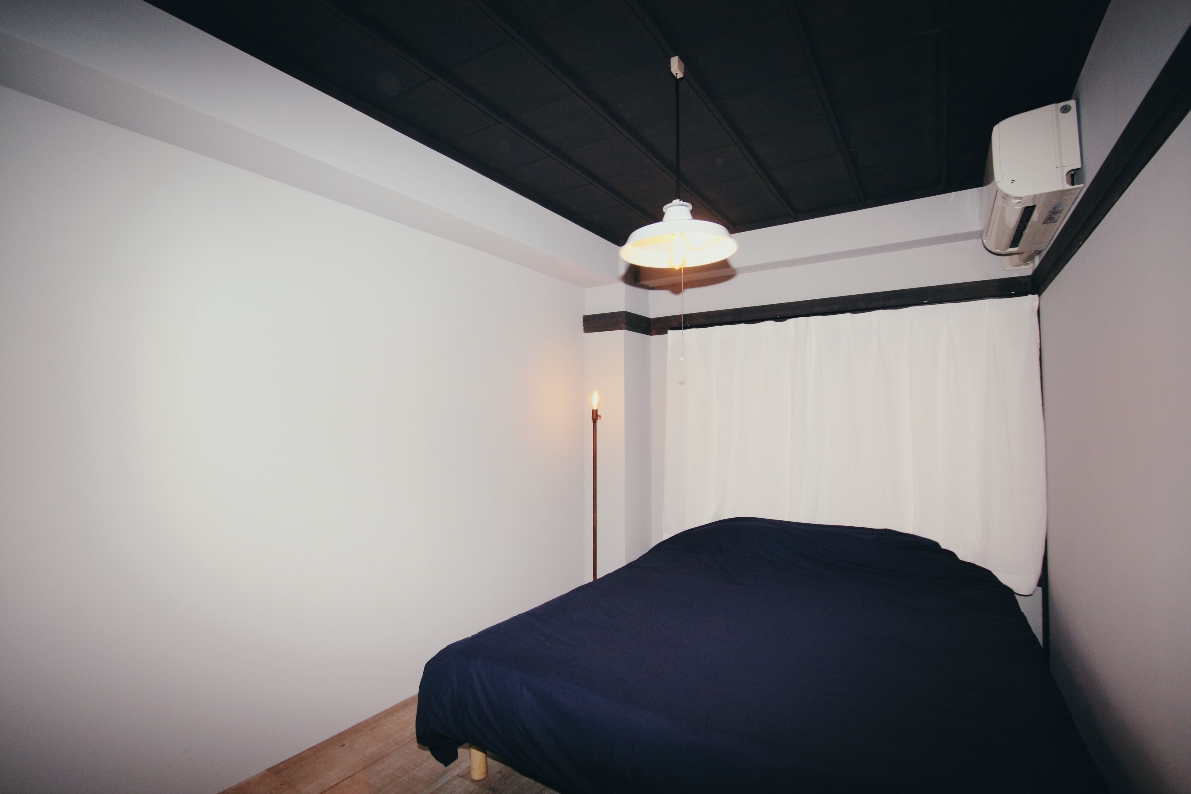 Un dormitorio con cama, lámpara colgante y aire acondicionado instalado en la pared.