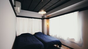 A room with two beds, a window with sheer curtains, a hanging light fixture, and a ceiling with exposed beams. - PITO BEPPU hostel & cafe (Beppu)