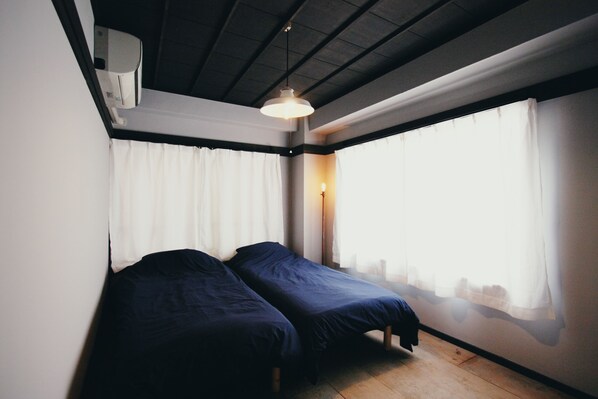 A room with two beds, a window with sheer curtains, a hanging light fixture, and a ceiling with exposed beams. - PITO BEPPU hostel & cafe (Beppu)