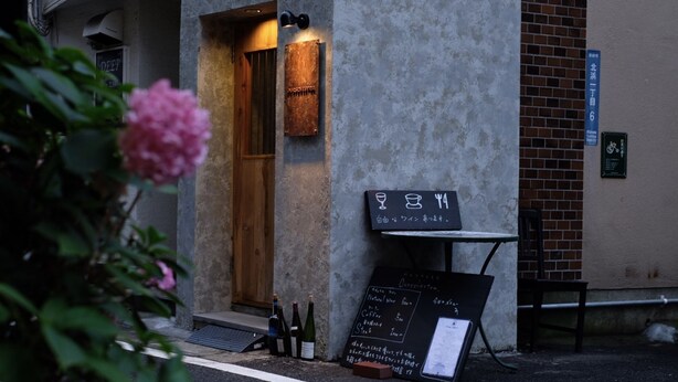 An outdoor seating area with a chalkboard menu, a wooden door, and a brick wall. - PITO BEPPU hostel & cafe (Beppu)