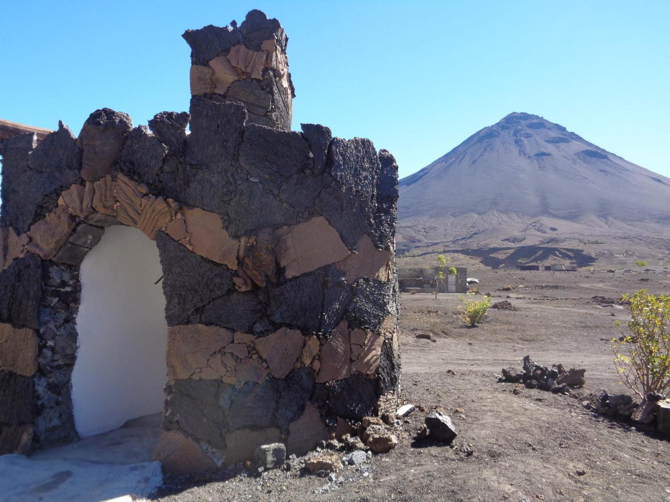 Een stenen structuur met een gedeeltelijk behouden deuropening, gelegen voor een kaal landschap en een berg.