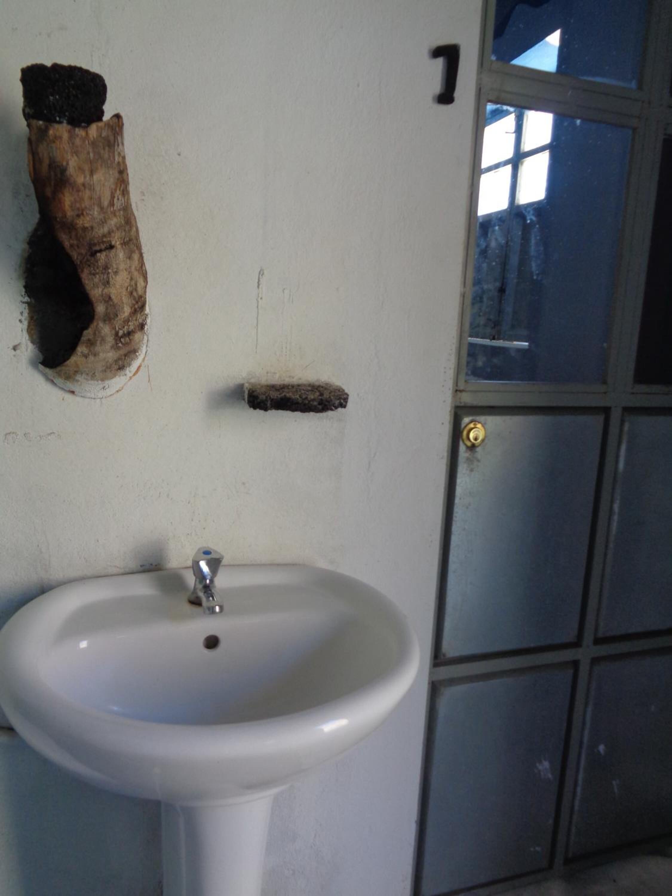 A white sink with a chrome faucet in a room with a plain white wall. There is a number '1' on the wall and a door with a window reflection.