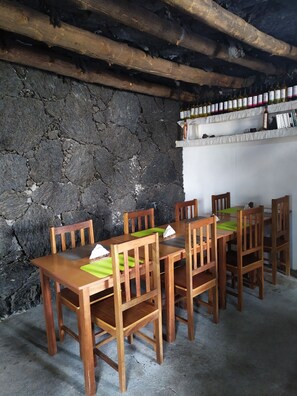 A rustic dining area with wooden tables and chairs, a stone wall, and a shelf with wine bottles. - Pensao Casa José Doce (Santa Catarina do Fogo)