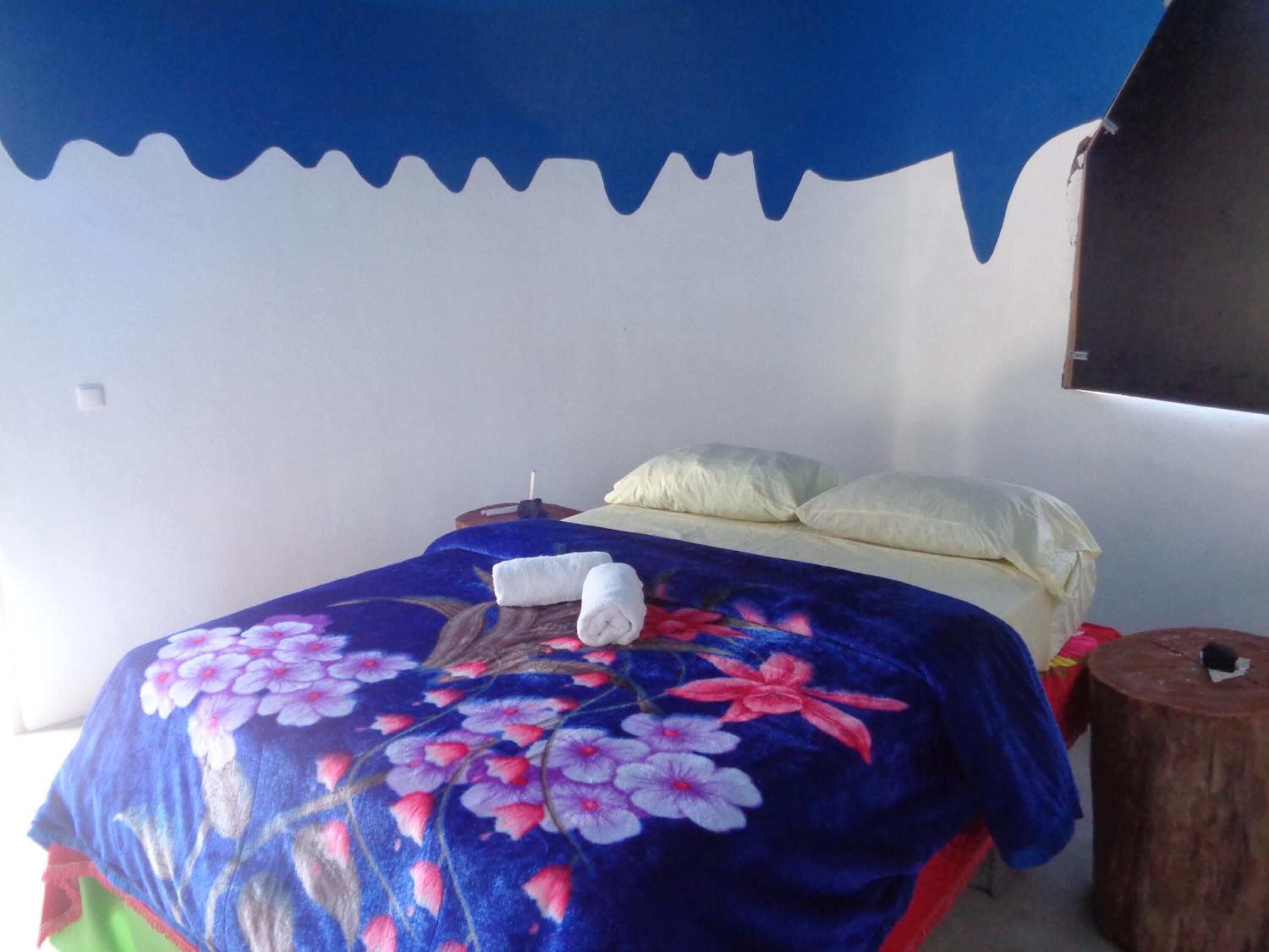 Una cama con una colcha estampada, una almohada blanca y un taburete de madera.
