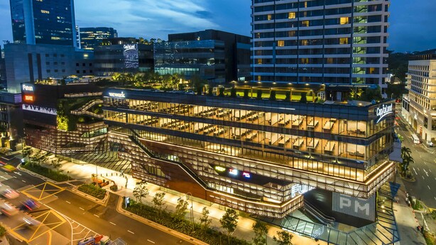 Un hotel a più piani con facciata in vetro, posti a sedere all'aperto e una scalinata ben visibile.