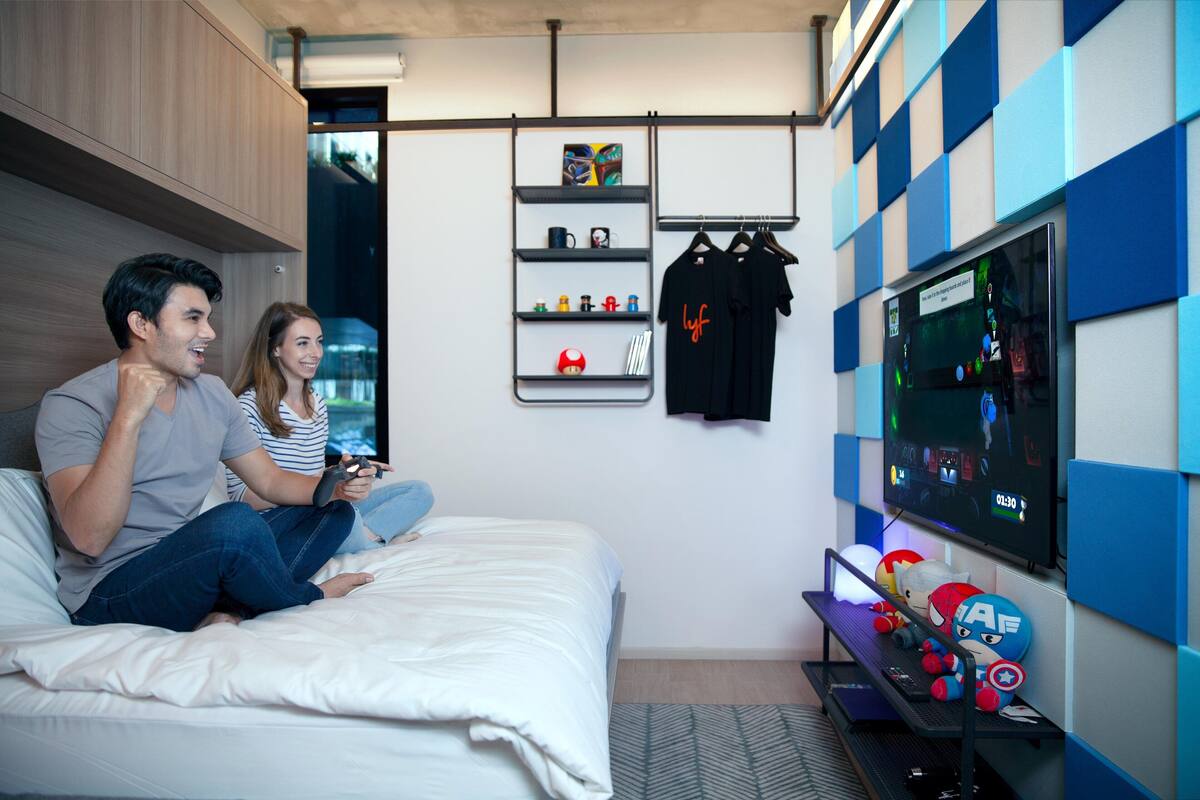 A bedroom with a bed, a TV on the wall, and a shelf with various items.