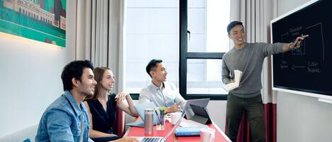 A meeting room with a large window, a blackboard with diagrams, and a table with laptops and coffee cups.