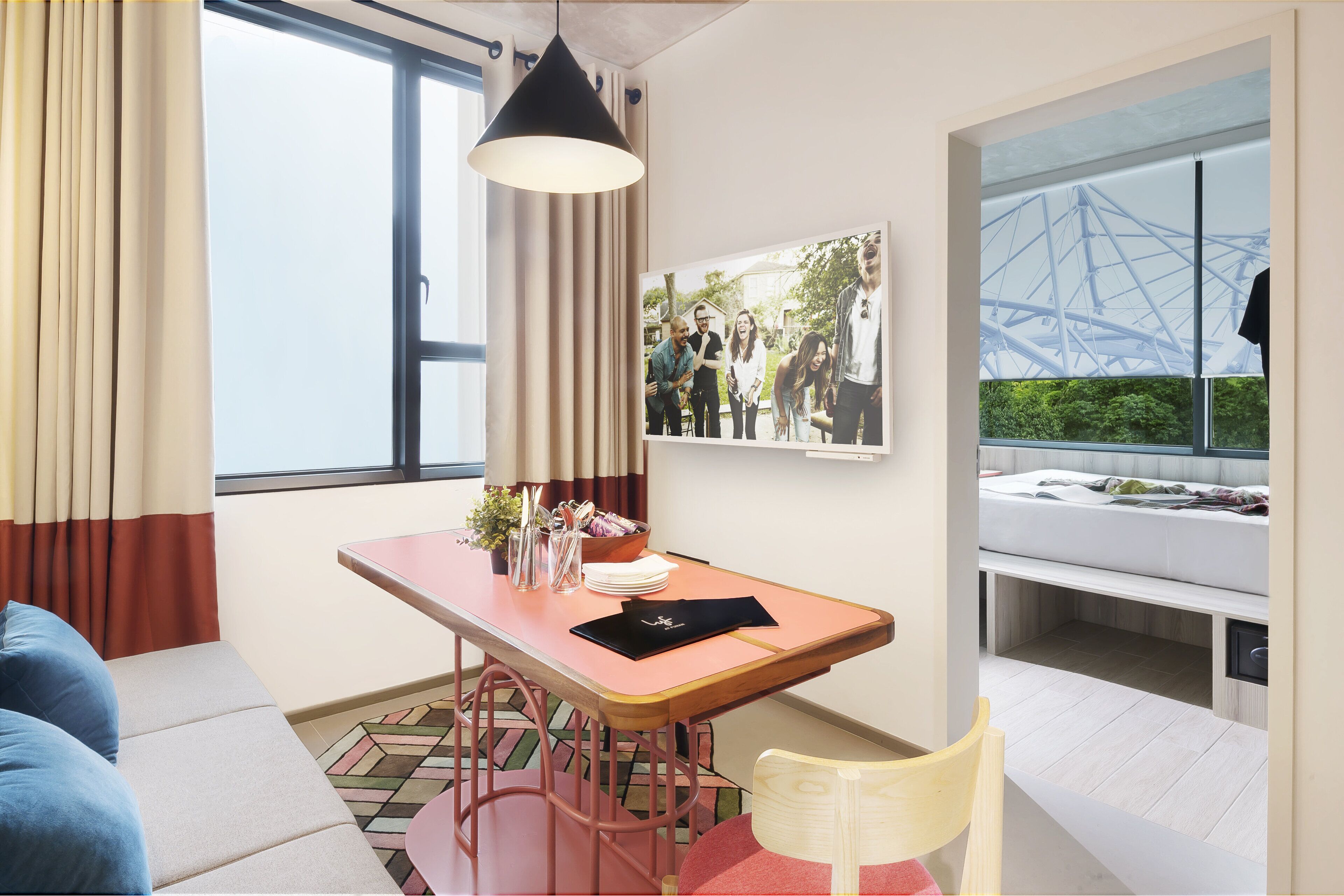 Una habitación de hotel moderna con sofá, una mesa de comedor con lámpara, cama con vista a un puente y una foto enmarcada en la pared.