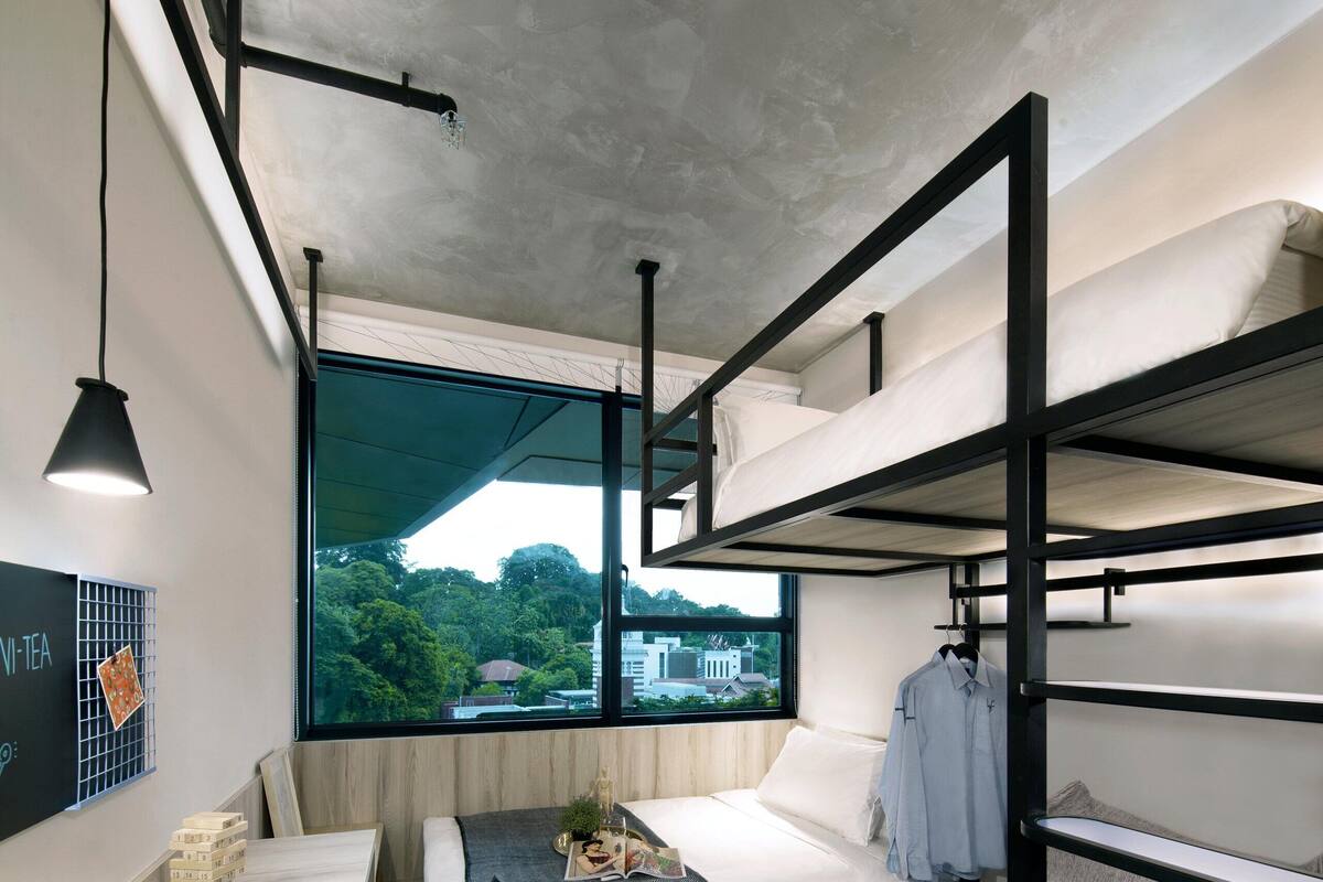 A modern room with bunk beds, a dining table, and a view of greenery outside.