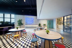 Un espace intérieur moderne avec des tables rondes et des tabourets, un panneau lumineux au néon et de grandes fenêtres.