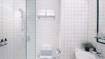 A modern bathroom with a glass-enclosed shower, a toilet, and a sink with a potted plant.