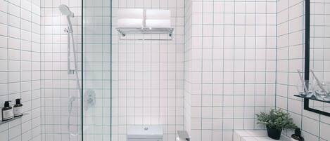 Un baño moderno con ducha de vidrio, inodoro y lavamanos con planta en maceta.