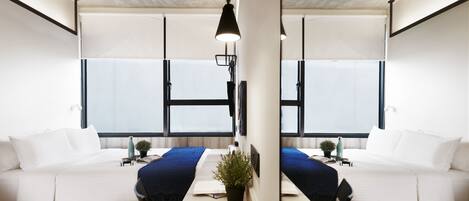 A modern, minimalist room with a central wooden table, two white sofas, and a large window providing natural light.