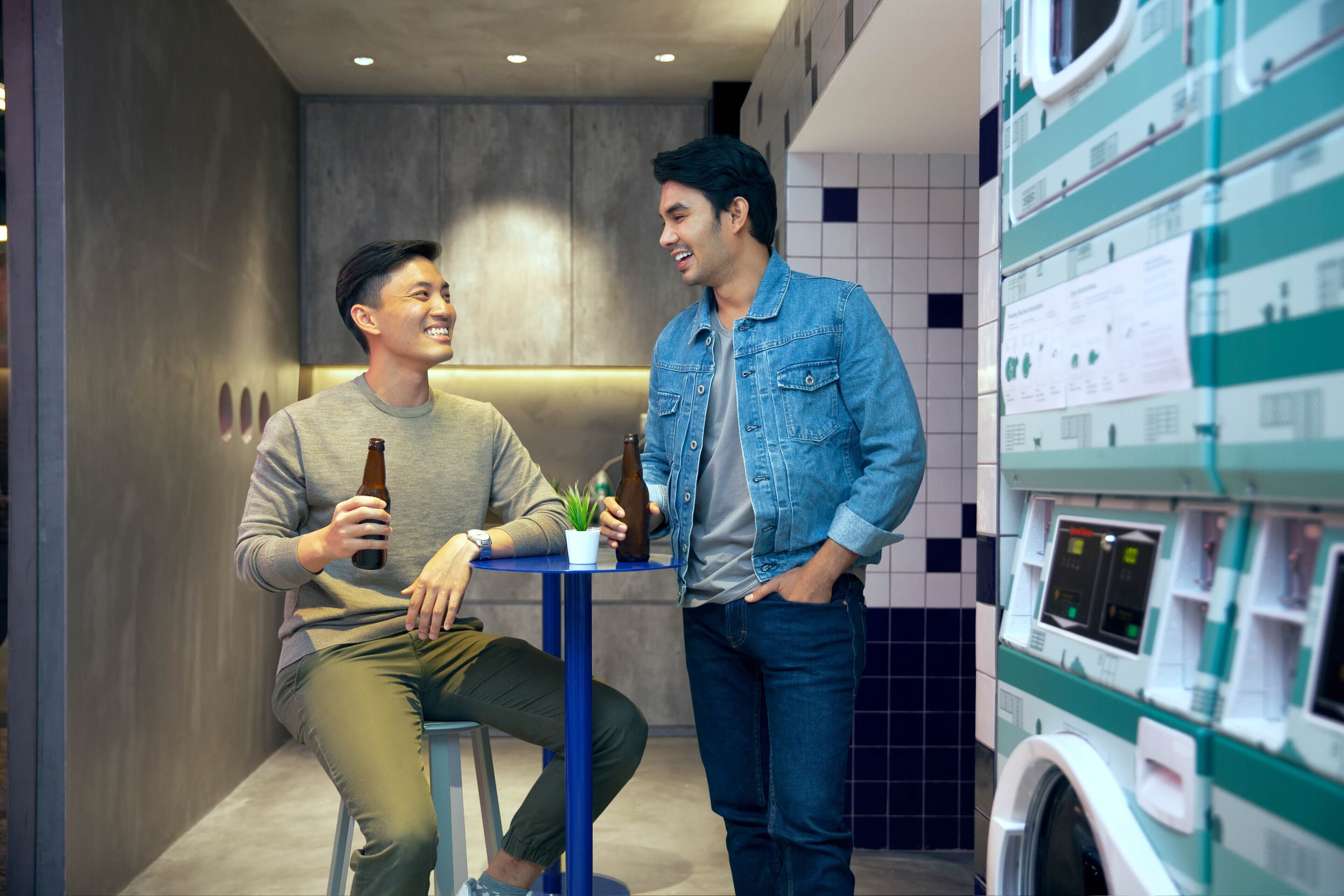 Two people sitting at a table in a modern room with a washing machine in the background.