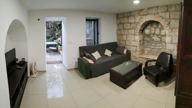 A living room with a sofa, a coffee table, and a TV. There is a stone wall and an arched window. - I'm Jerusalem (Jerusalem)