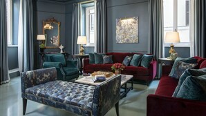 A room with a red sofa, blue armchairs, a coffee table with chess, and a chandelier. - Rocco Forte House Piazza di Spagna Roma (Rome)