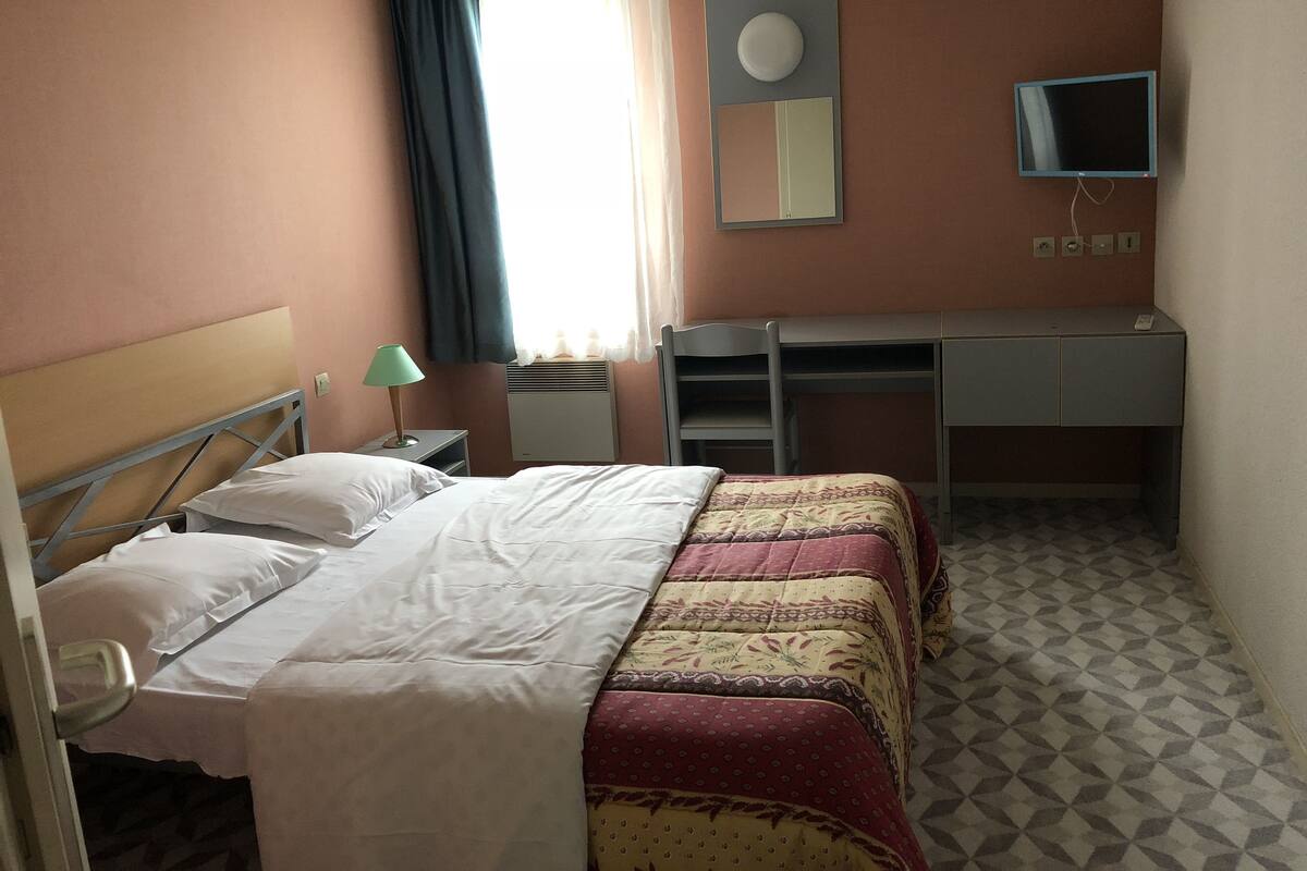 Une chambre d’hôtel équipée d’un lit, d’un bureau, d’une chaise, d’une télévision et d’une fenêtre avec des rideaux.