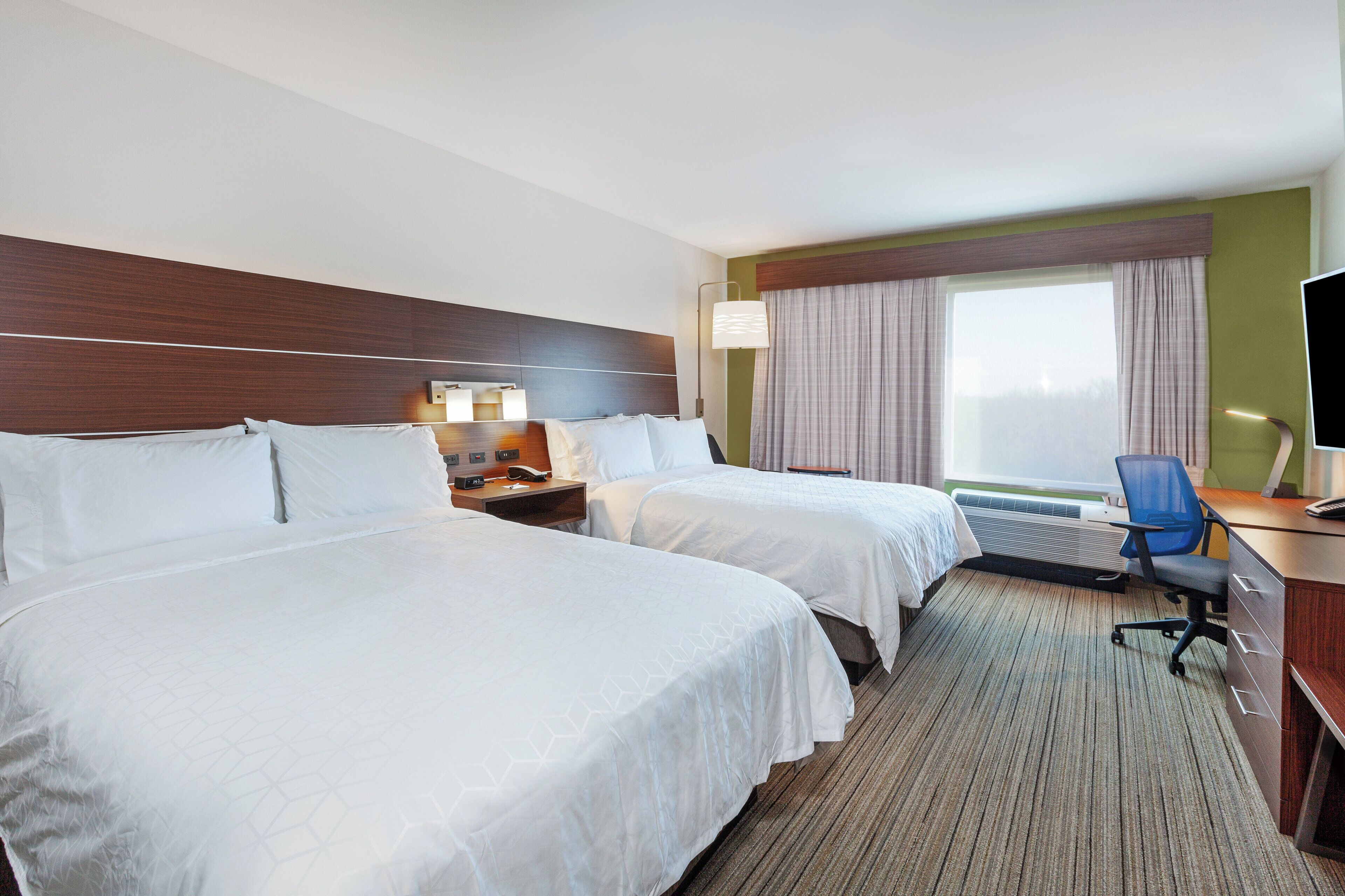 A hotel room with two beds, a desk, a chair, a TV, and a window with curtains.