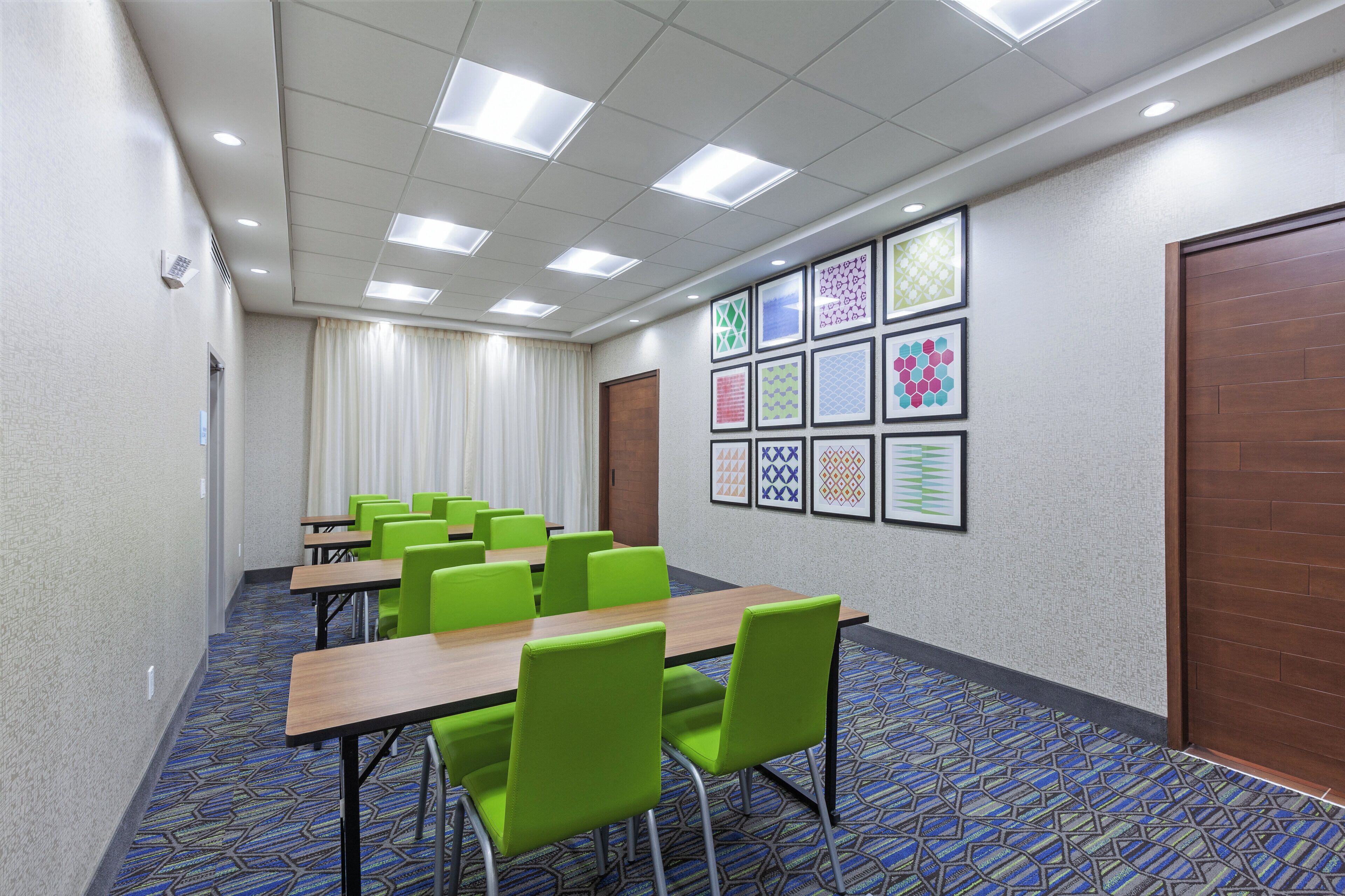 A conference room with tables and chairs, a patterned carpet, and a wall with framed artwork.