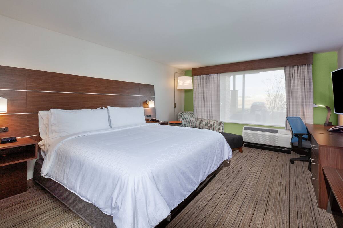 A hotel room with a large bed, a desk, a chair, a TV, and a window with curtains.