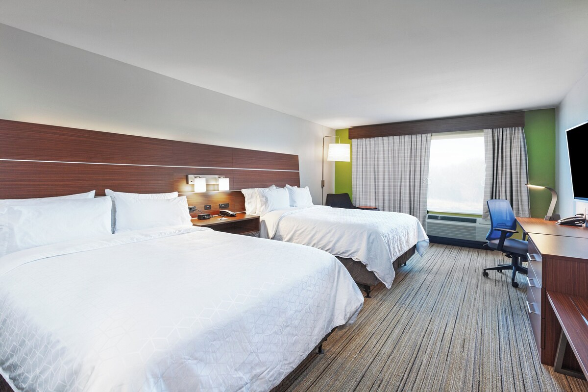 A hotel room with two beds, a desk with a chair, a TV, and a window with curtains.