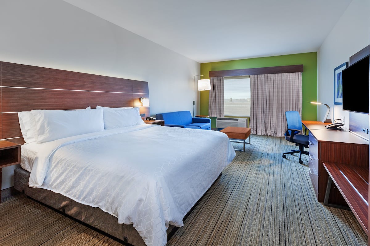 A hotel room with a large bed, a desk, a chair, and a television.