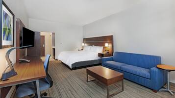 Een hotelkamer met een bed, een bureau met een computer, een blauwe bank, een klein tafeltje en een aan de muur bevestigde televisie.