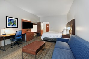 A hotel room with a bed, a desk, a chair, a sofa, a TV, and a framed picture on the wall.