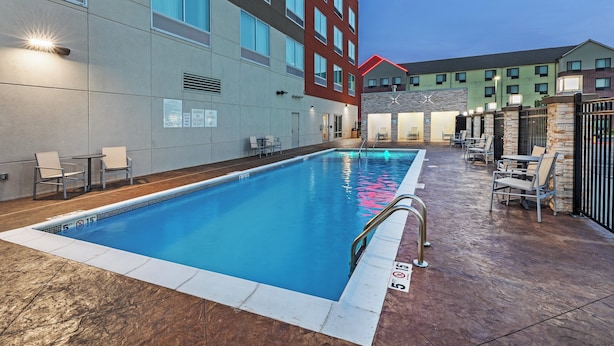 A swimming pool with a clear blue water, surrounded by a patio area with chairs and tables. - Holiday Inn Express & Suites Tulsa Northeast - Owasso by IHG (Owasso)