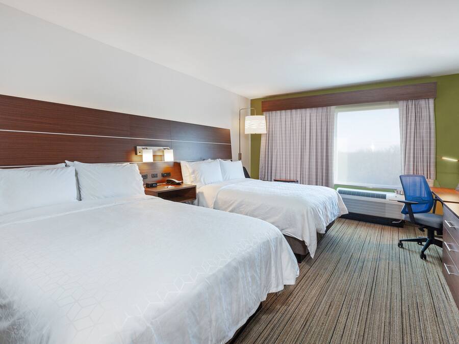 A hotel room with two beds, a desk, a chair, a TV, and a window with curtains.