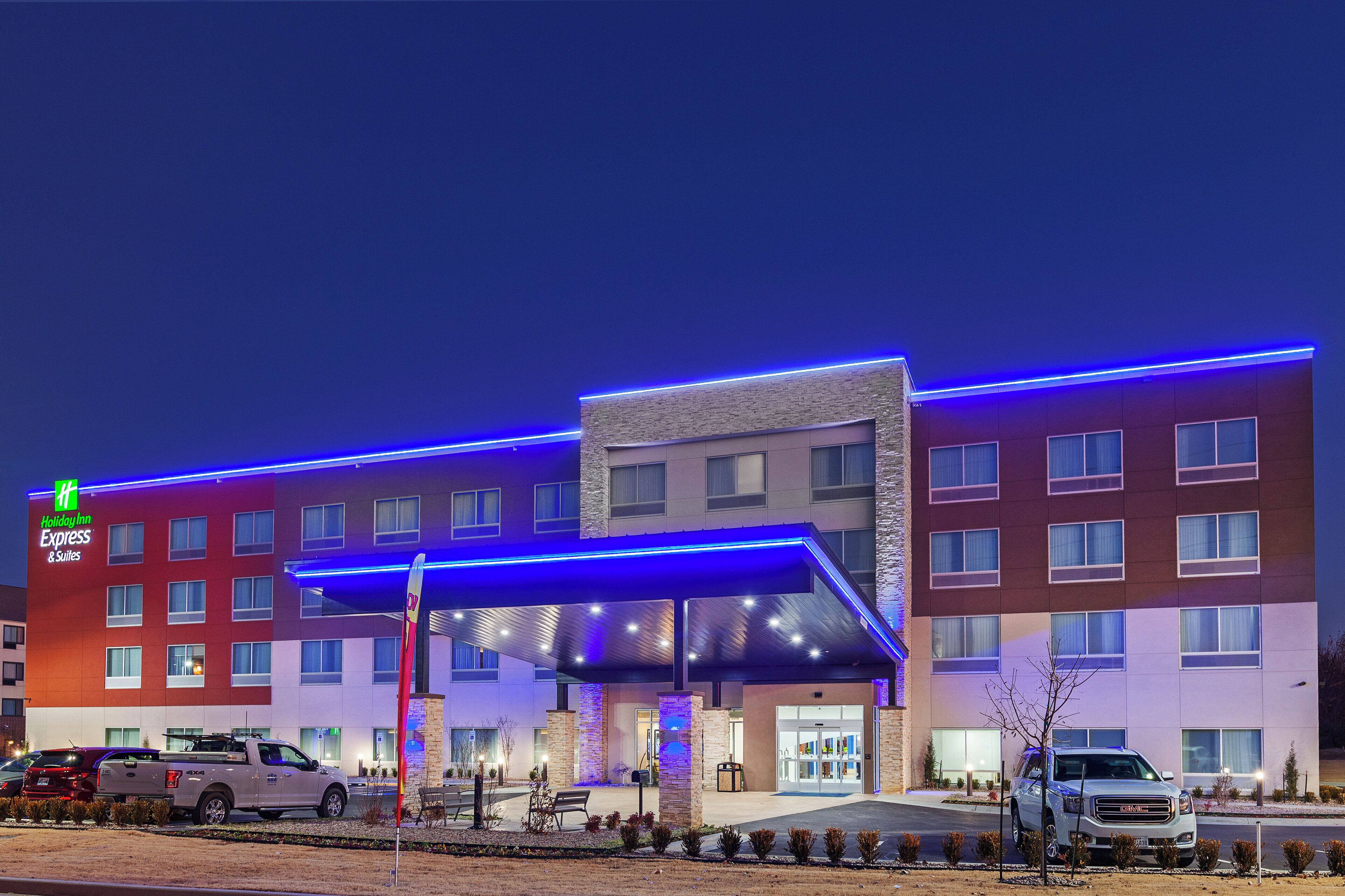 A Holiday Inn Express & Suites hotel with a modern design, featuring a covered entrance and a parking lot with vehicles.
