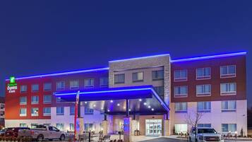 A Holiday Inn Express & Suites hotel with a modern design, featuring a covered entrance and a parking lot with vehicles.