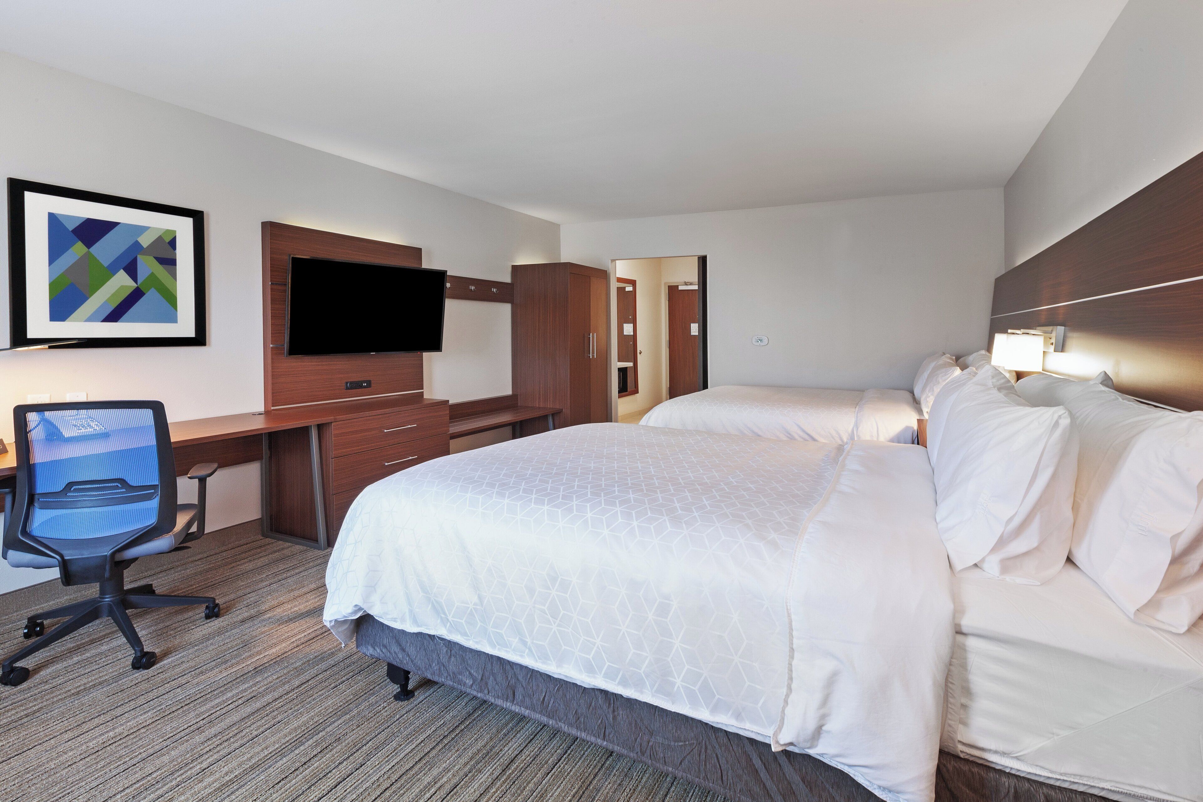 A hotel room with a bed, desk, chair, TV, and artwork on the wall.