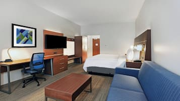 A hotel room with a bed, a desk with a chair, a sofa, a TV, and a framed picture on the wall.