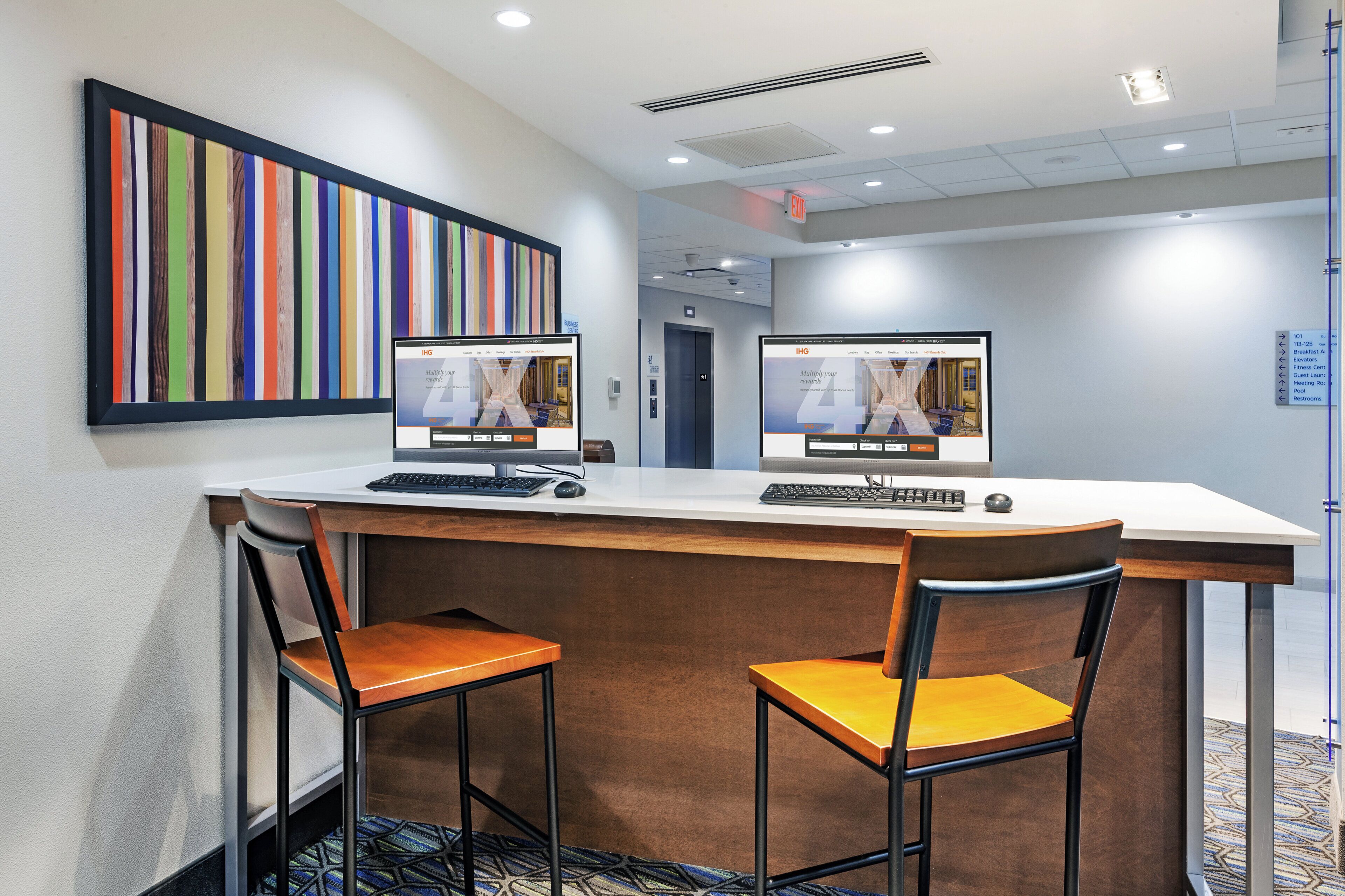 A hotel reception desk with two computer monitors, a framed artwork, and a carpeted floor.