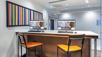 A hotel reception desk with two computer monitors, a framed artwork, and a carpeted floor.