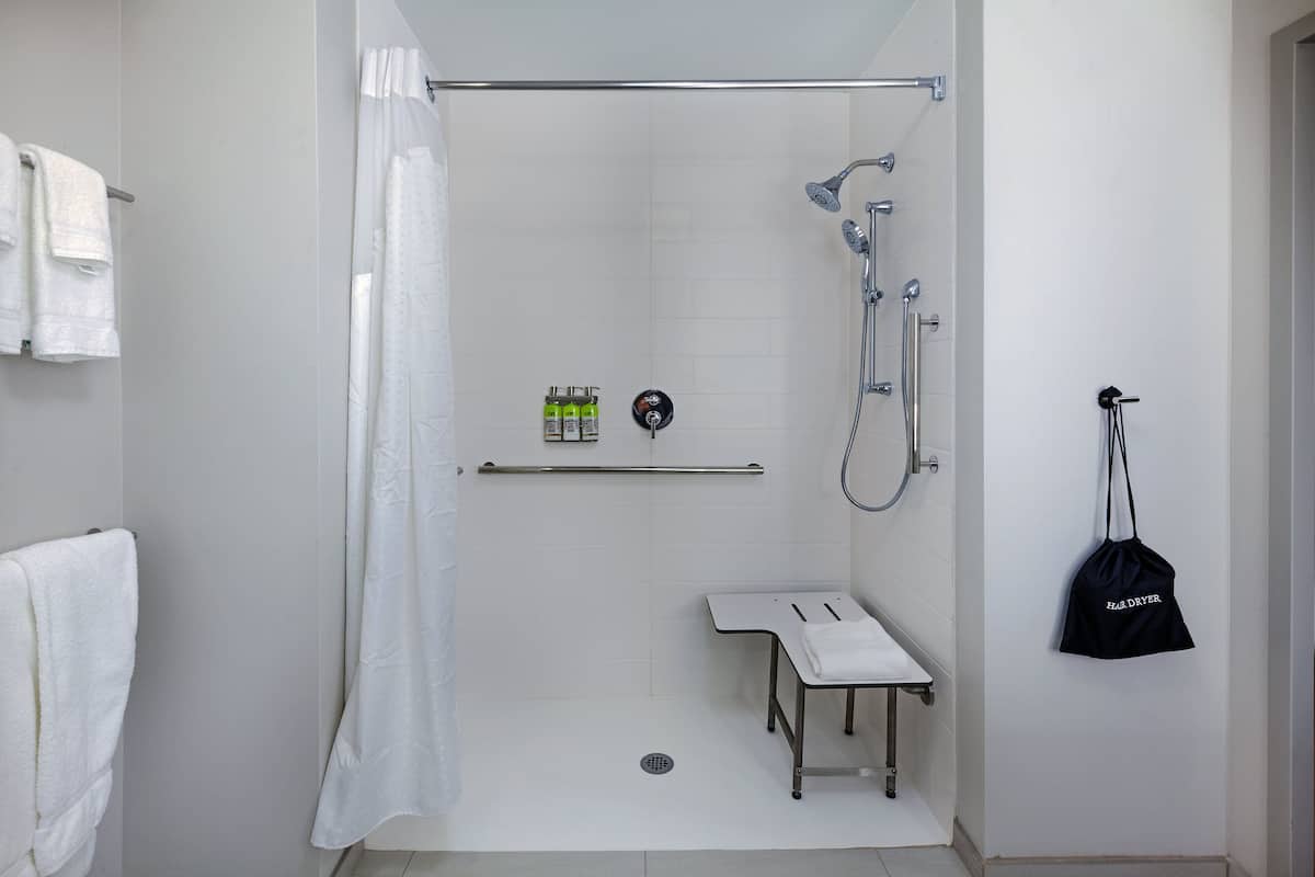 A modern bathroom with a shower, a towel rack, a bench, and a hairdryer hanging on the wall.