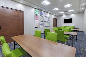 Una sala de conferències amb diverses taules i cadires, un televisor penjat a la paret i quadres amb marc.