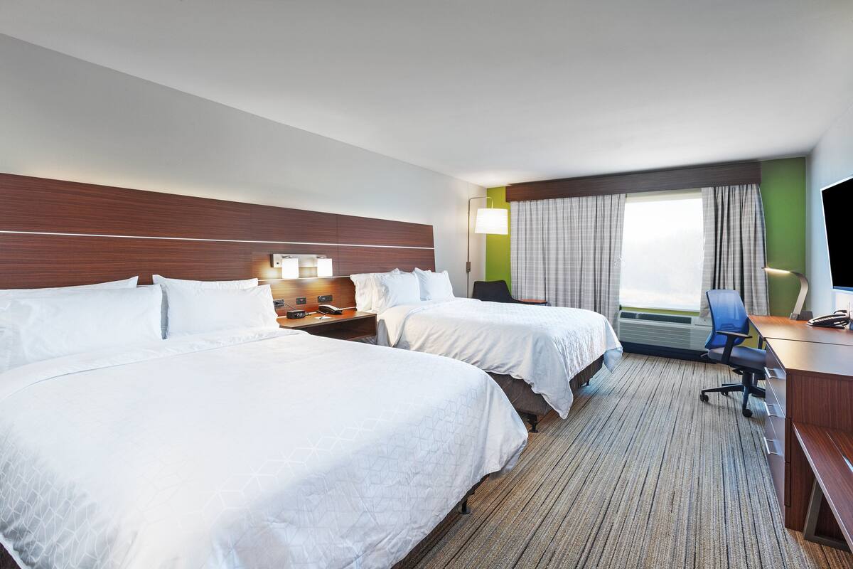 A hotel room with two beds, a desk with a chair, a TV, and a window with curtains.
