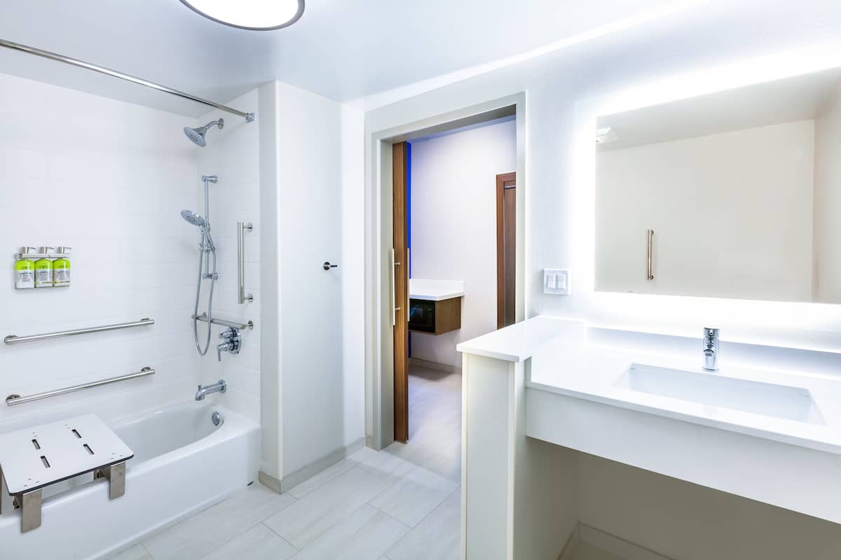 A modern bathroom with a walk-in shower, grab bars, a large mirror, and a sink.