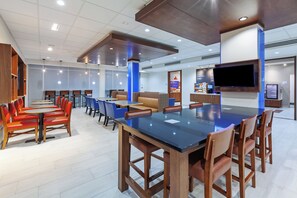 A modern restaurant with a large central table, booths, and a flat-screen TV. - Holiday Inn Express & Suites Tulsa Northeast - Owasso by IHG (Owasso)