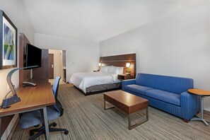A hotel room with a bed, a sofa, a desk with a computer, and a TV.