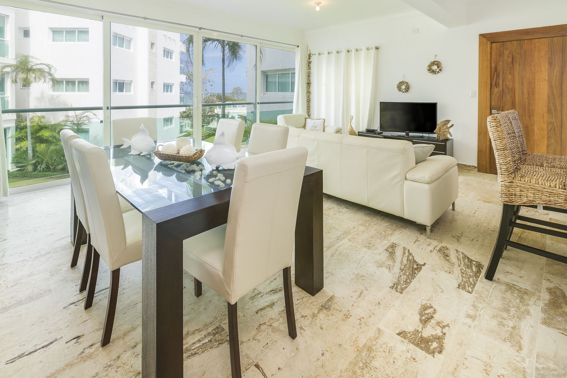 A modern living room with a glass dining table, white sofas, and a TV.