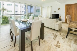 A modern living room with a glass dining table, white sofas, and a TV. - Escondido Bay Properties by Caribe Stays (Sosúa)