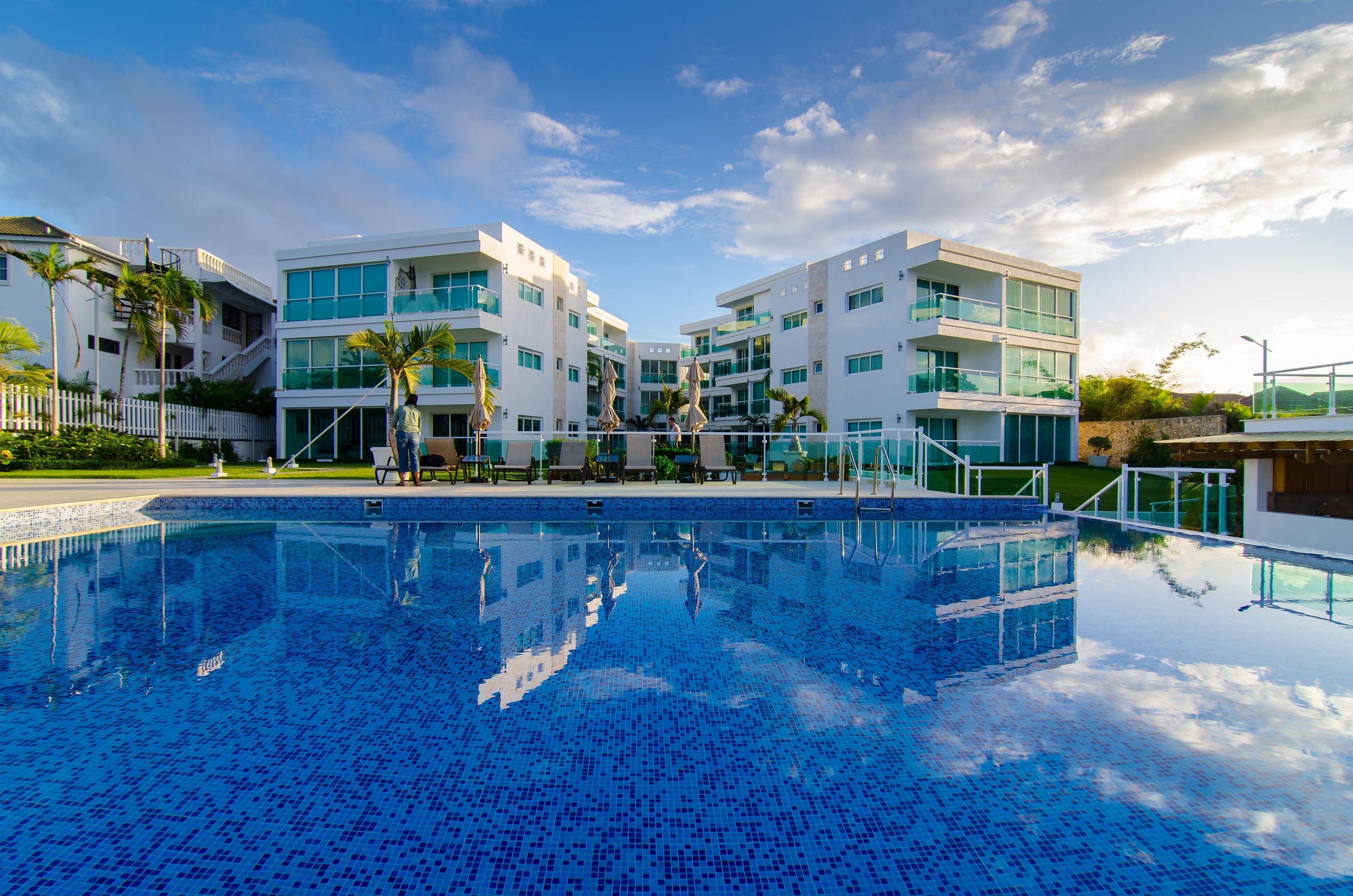 A modern hotel with a swimming pool, multiple balconies, and a white fence.