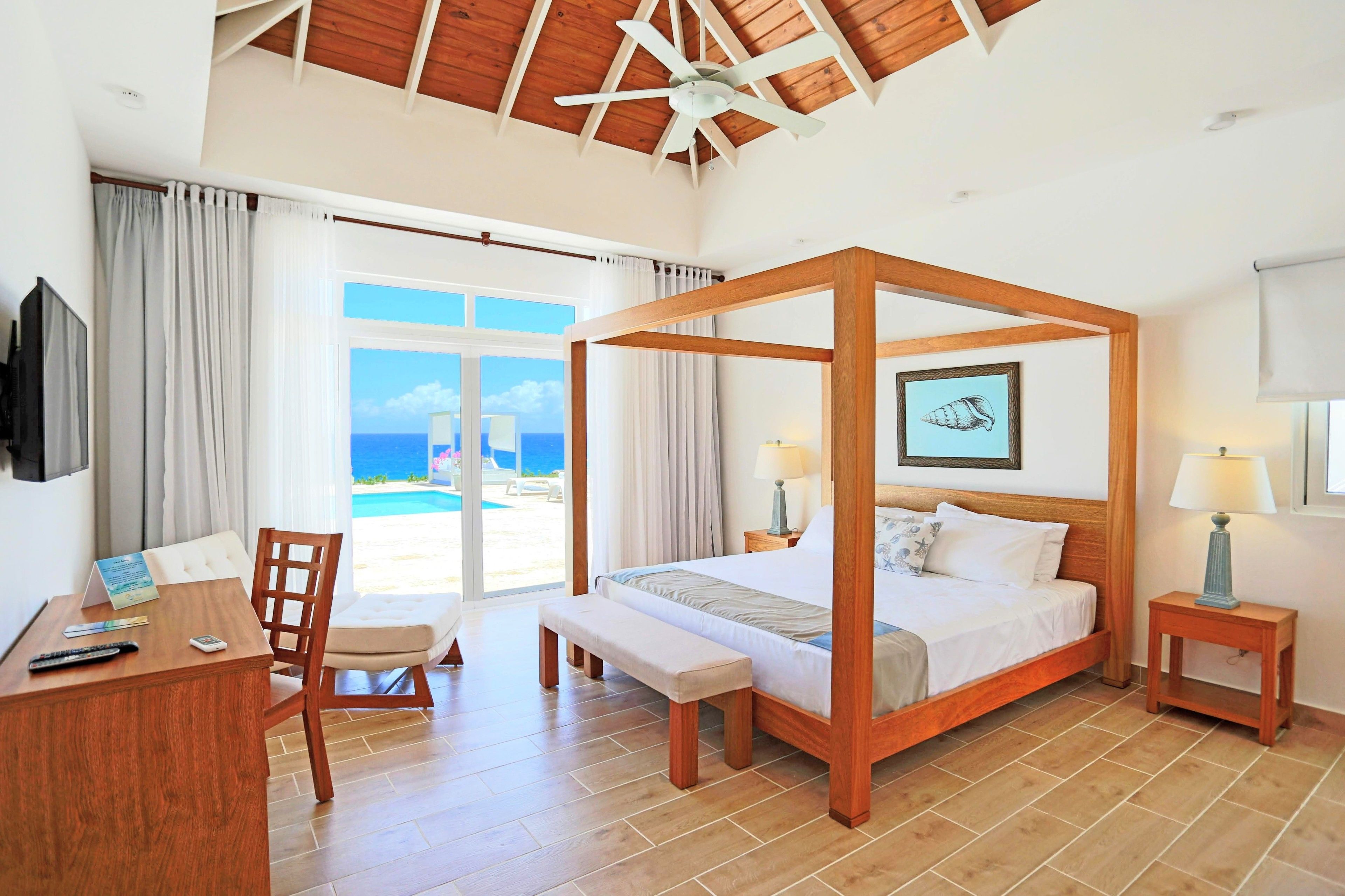 Una cama con dosel con vistas al mar, un escritorio con una silla y una mesita de noche con una lámpara.